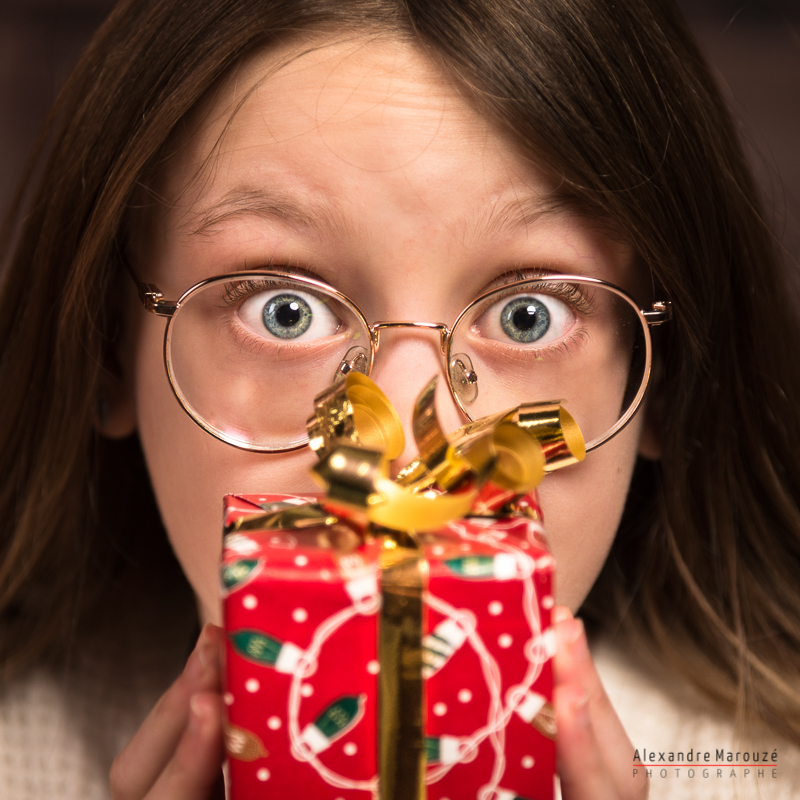 portrait de jeune fille aux yeux bleus tenant un paquet cadeau devant le visage